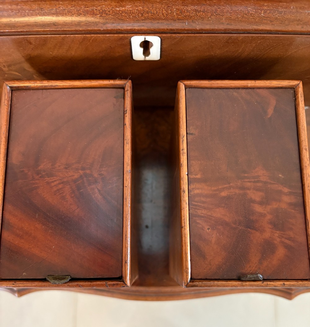 A Regency mahogany tea caddy featuring a hinged lid, tapered body, central escutcheon, and metal ball feet. View II