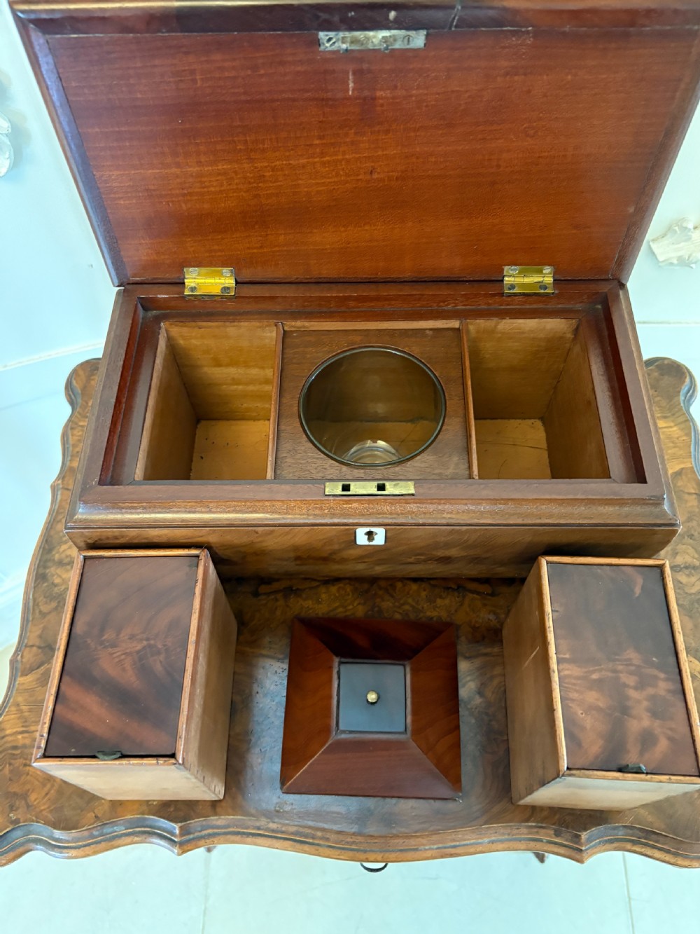 A Regency mahogany tea caddy featuring a hinged lid, tapered body, central escutcheon, and metal ball feet. View VII