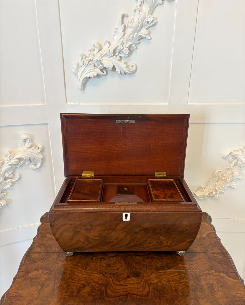 A Regency mahogany tea caddy featuring a hinged lid, tapered body, central escutcheon, and metal ball feet. View XI
