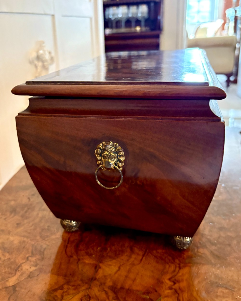 A Regency mahogany tea caddy featuring a hinged lid, tapered body, central escutcheon, and metal ball feet. View XVIII