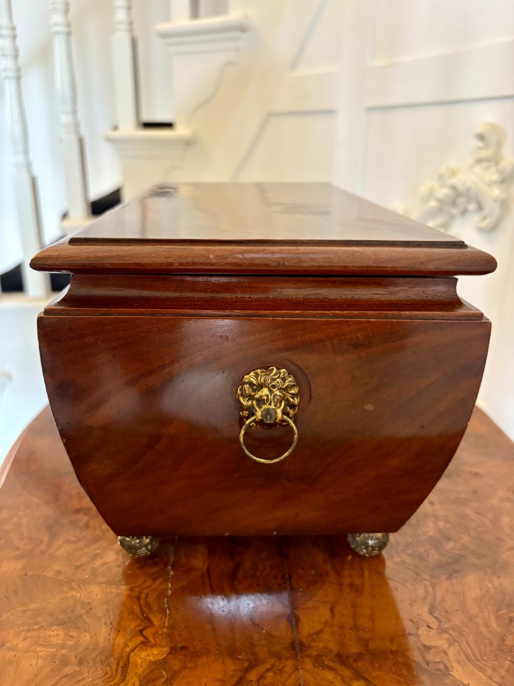 A Regency mahogany tea caddy featuring a hinged lid, tapered body, central escutcheon, and metal ball feet. View XIX
