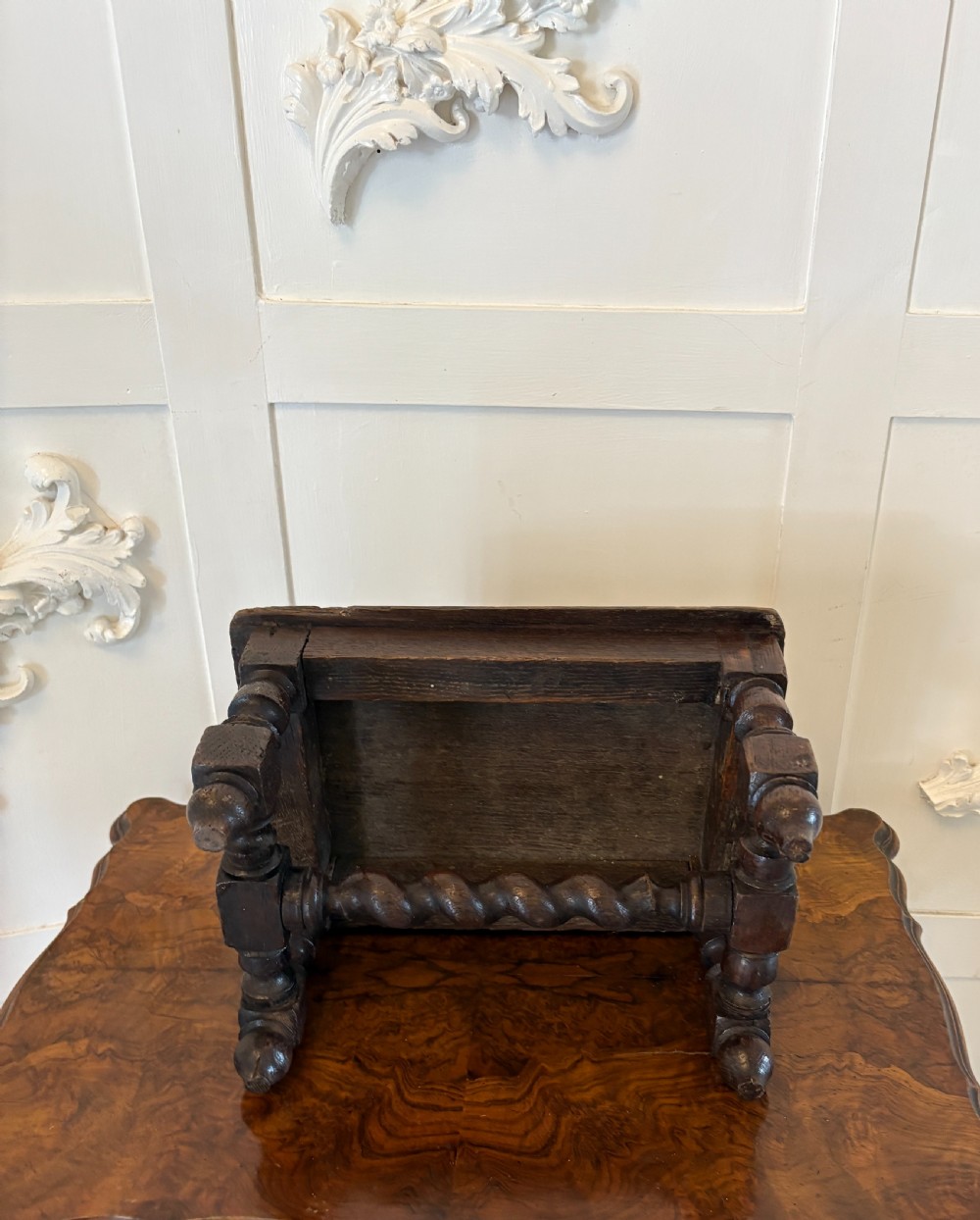 A dark carved oak miniature table with a central carved flower motif on top, carved frieze edges, turned legs, and a barley twist cross stretcher. View V