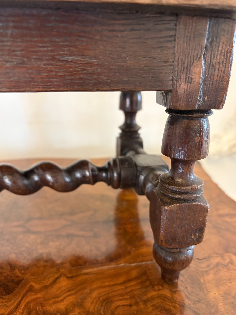 A dark carved oak miniature table with a central carved flower motif on top, carved frieze edges, turned legs, and a barley twist cross stretcher. View VI