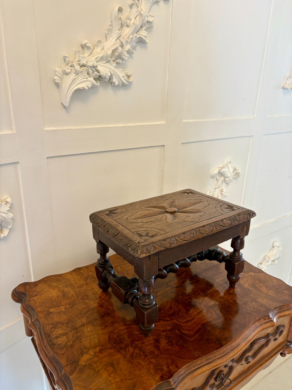 A dark carved oak miniature table with a central carved flower motif on top, carved frieze edges, turned legs, and a barley twist cross stretcher. View VII