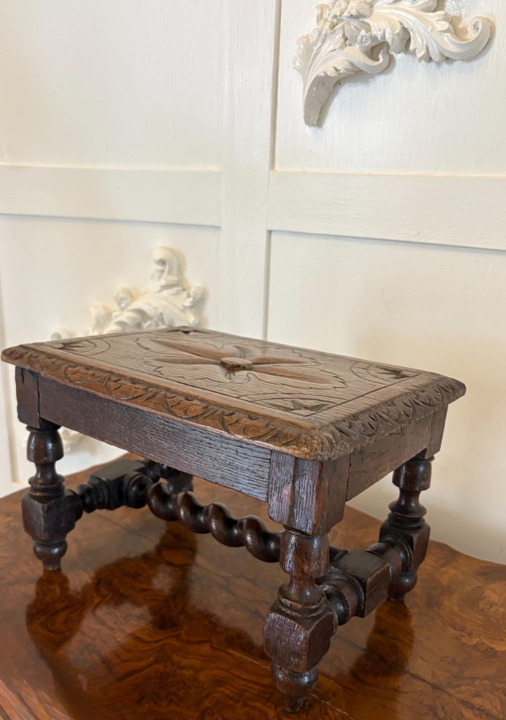 A dark carved oak miniature table with a central carved flower motif on top, carved frieze edges, turned legs, and a barley twist cross stretcher. View VIII
