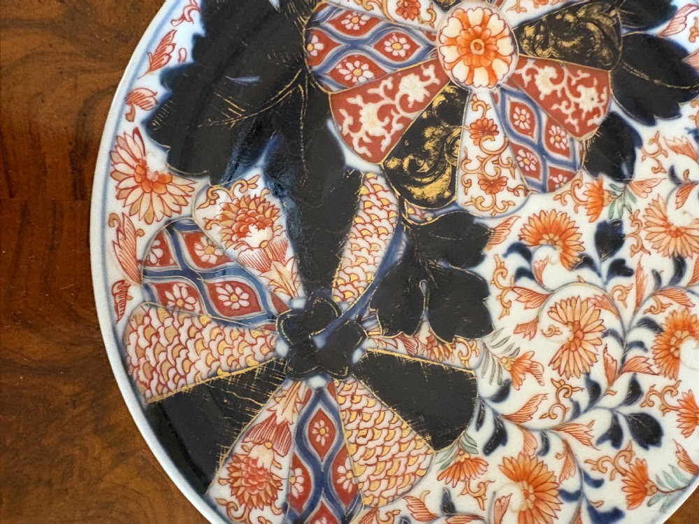 A circular antique Japanese Imari porcelain plate hand-painted with intricate cobalt blue, rust-red, and gilt floral patterns. View IX