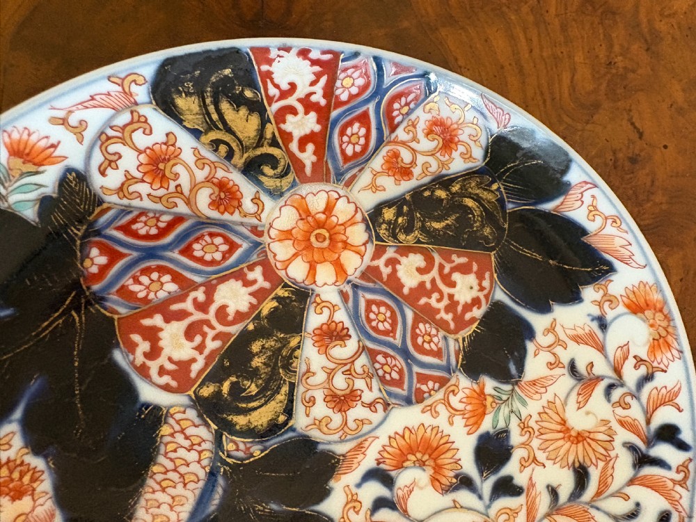 A circular antique Japanese Imari porcelain plate hand-painted with intricate cobalt blue, rust-red, and gilt floral patterns. View X