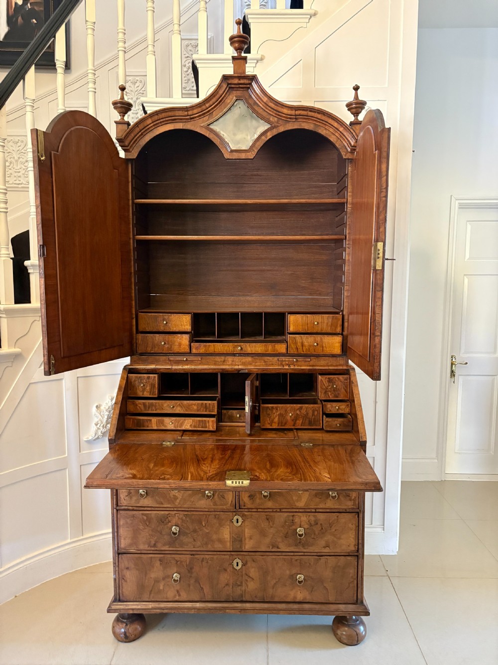 A Queen Anne style burr walnut bureau bookcase featuring a double-arched mirror door top section above a slant-front writing bureau and graduated drawers. View XVI