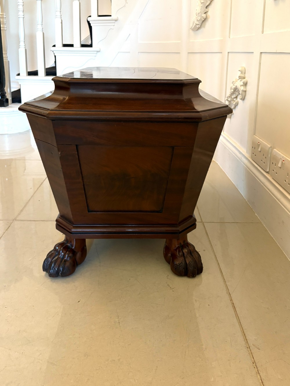 A Regency mahogany wine cooler shaped as a classical sarcophagus with figured wood panels, a central brass keyhole, and carved lion paw feet. View IV