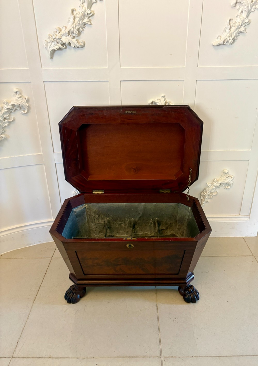 A Regency mahogany wine cooler shaped as a classical sarcophagus with figured wood panels, a central brass keyhole, and carved lion paw feet. View IX