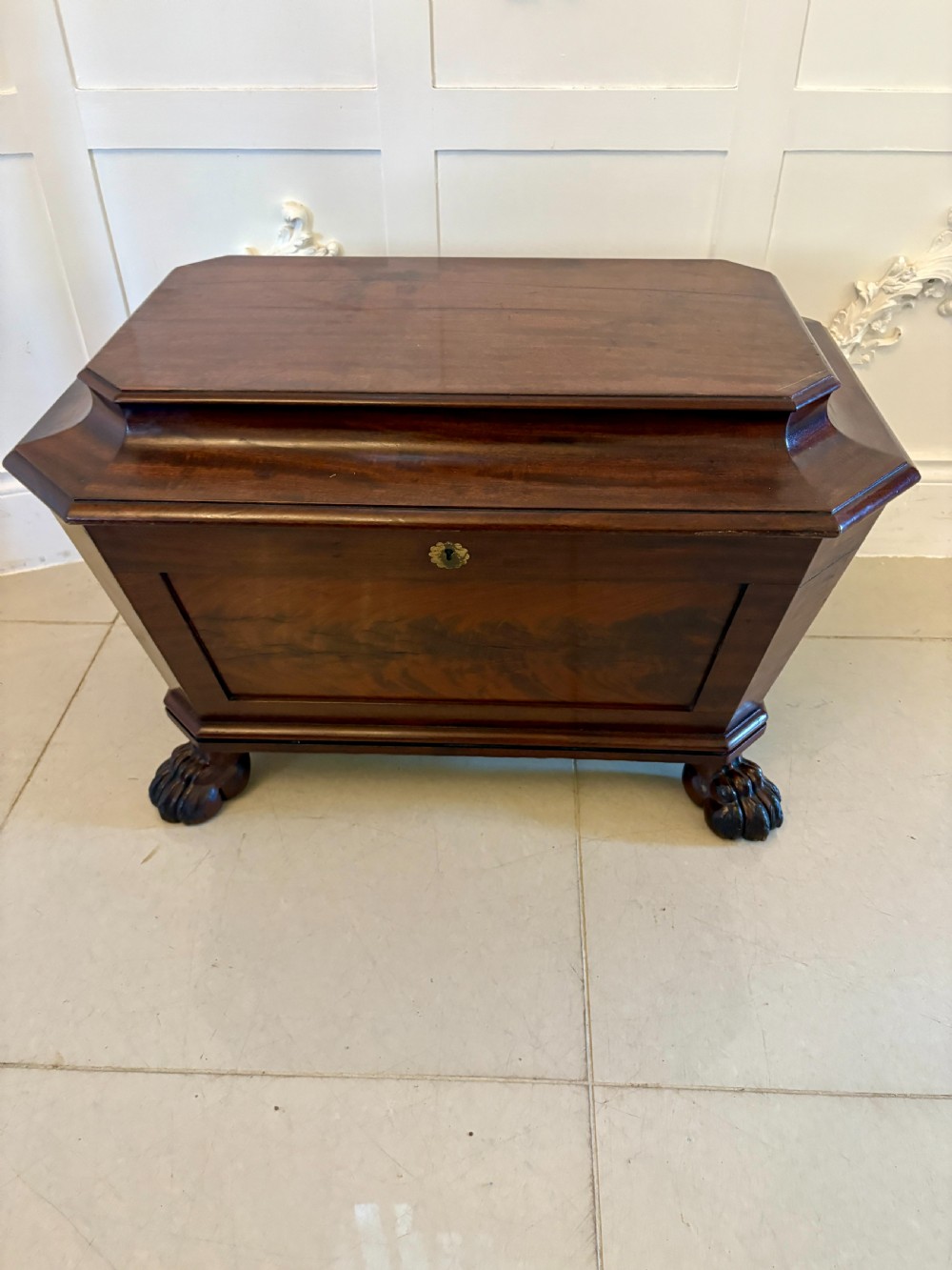 A Regency mahogany wine cooler shaped as a classical sarcophagus with figured wood panels, a central brass keyhole, and carved lion paw feet. View XIV