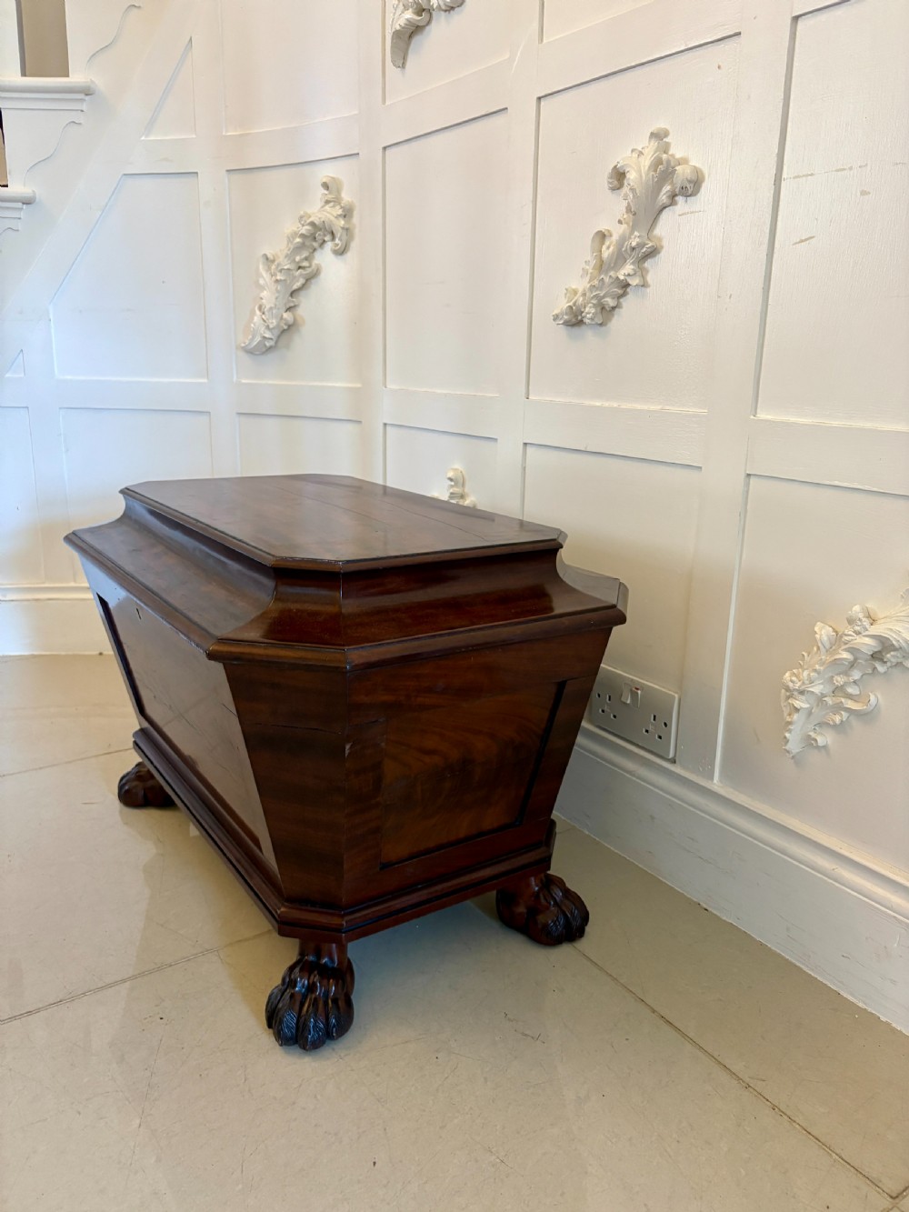 A Regency mahogany wine cooler shaped as a classical sarcophagus with figured wood panels, a central brass keyhole, and carved lion paw feet. View XVI