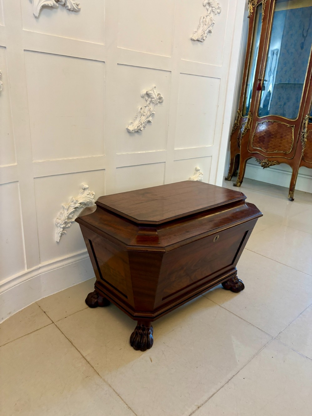 A Regency mahogany wine cooler shaped as a classical sarcophagus with figured wood panels, a central brass keyhole, and carved lion paw feet. View XVII