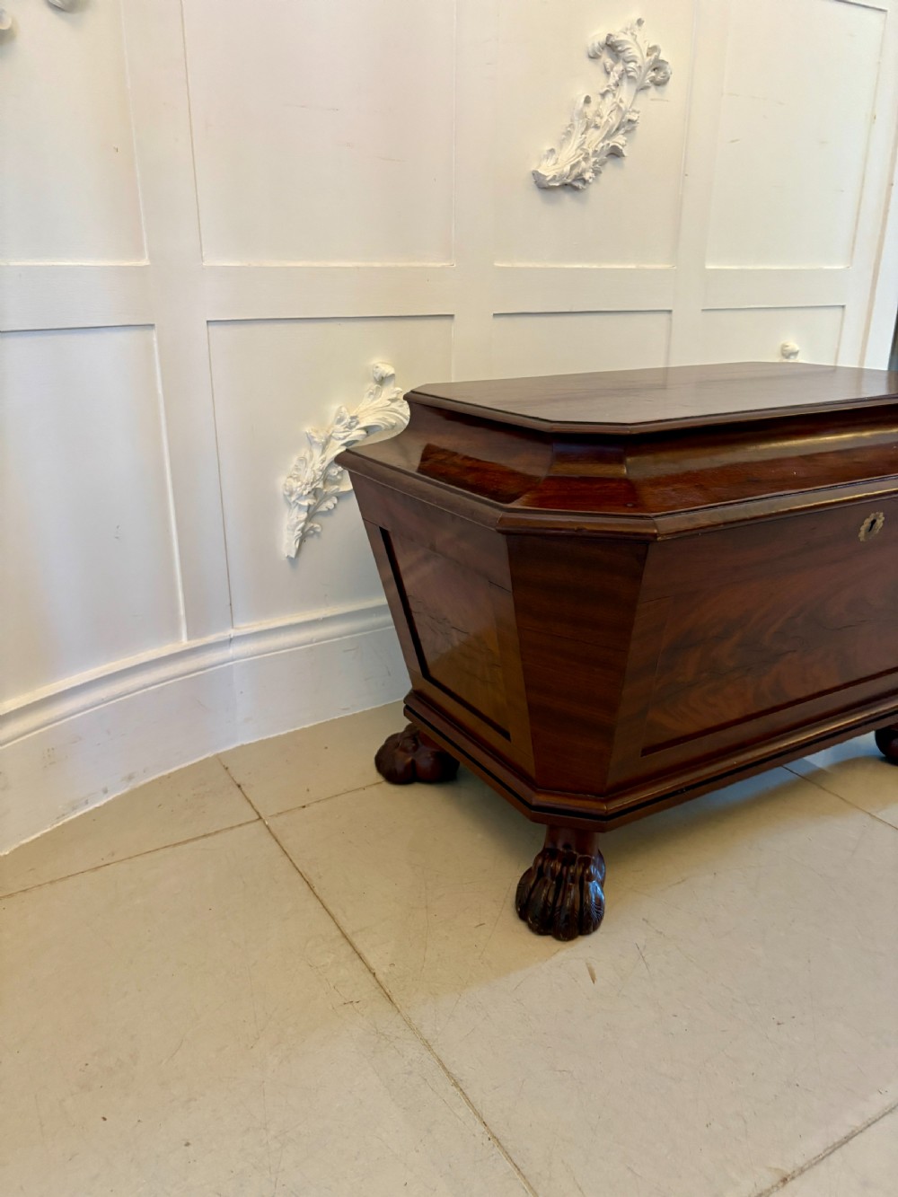 A Regency mahogany wine cooler shaped as a classical sarcophagus with figured wood panels, a central brass keyhole, and carved lion paw feet. View XVIII