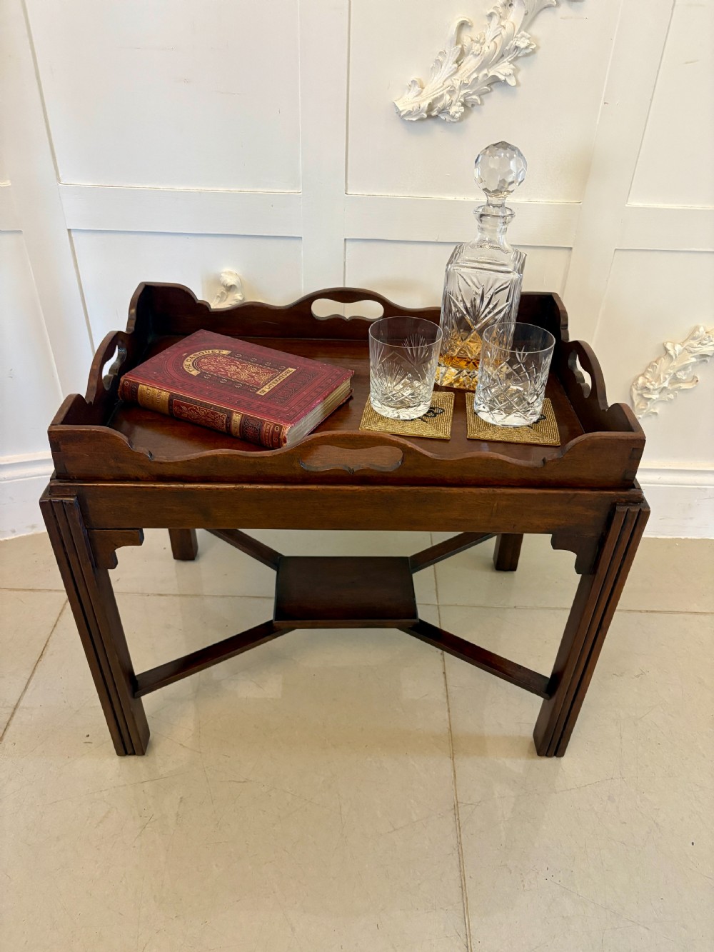 An Edwardian mahogany butlers tray featuring scalloped gallery sides with cut-out handles, resting on a matching wooden stand with reeded legs and cross-stretchers. View VIII