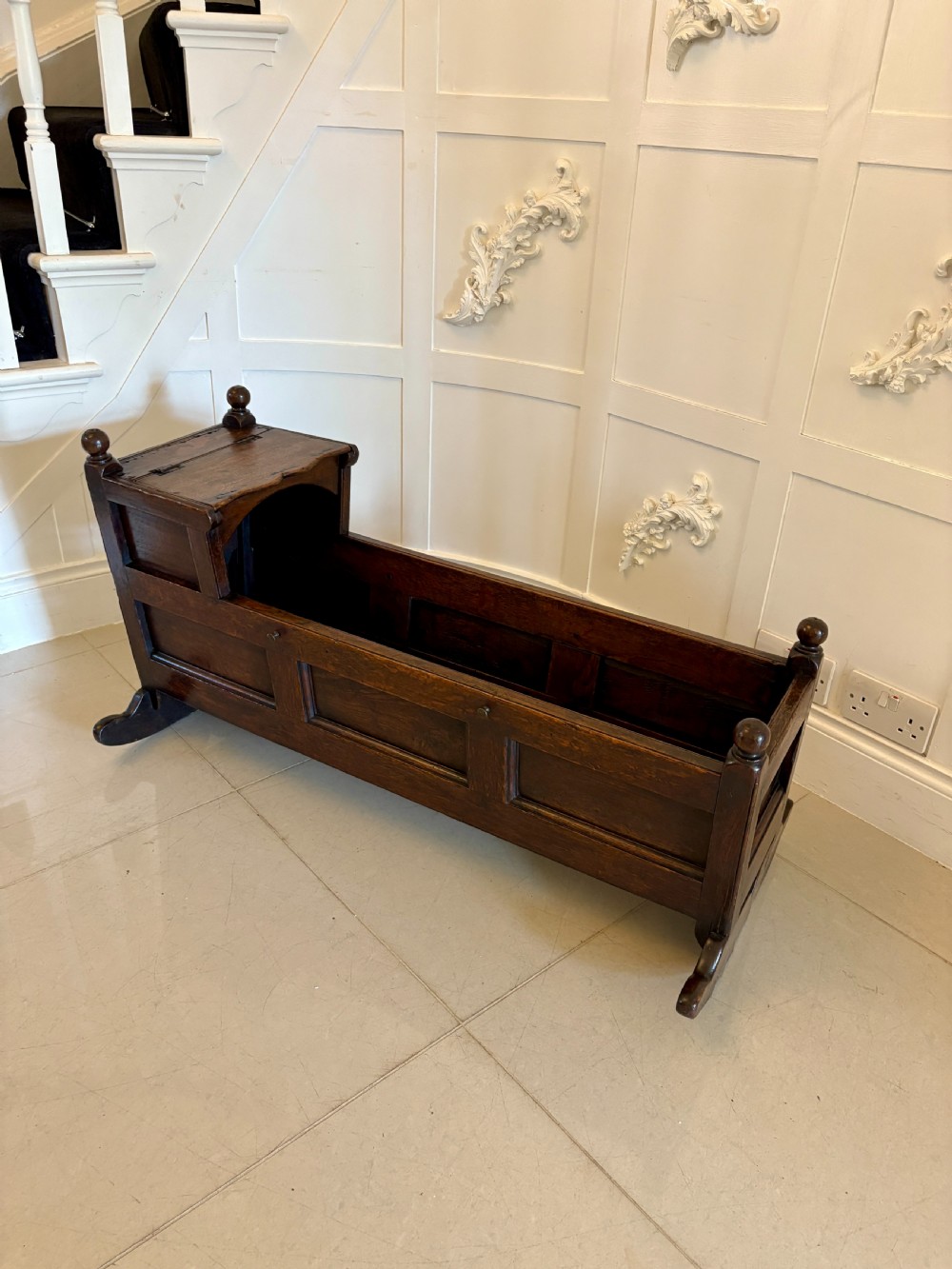 A dark oak panelled rocking crib featuring a hooded end, raised corner finials, and curved rocking runners.