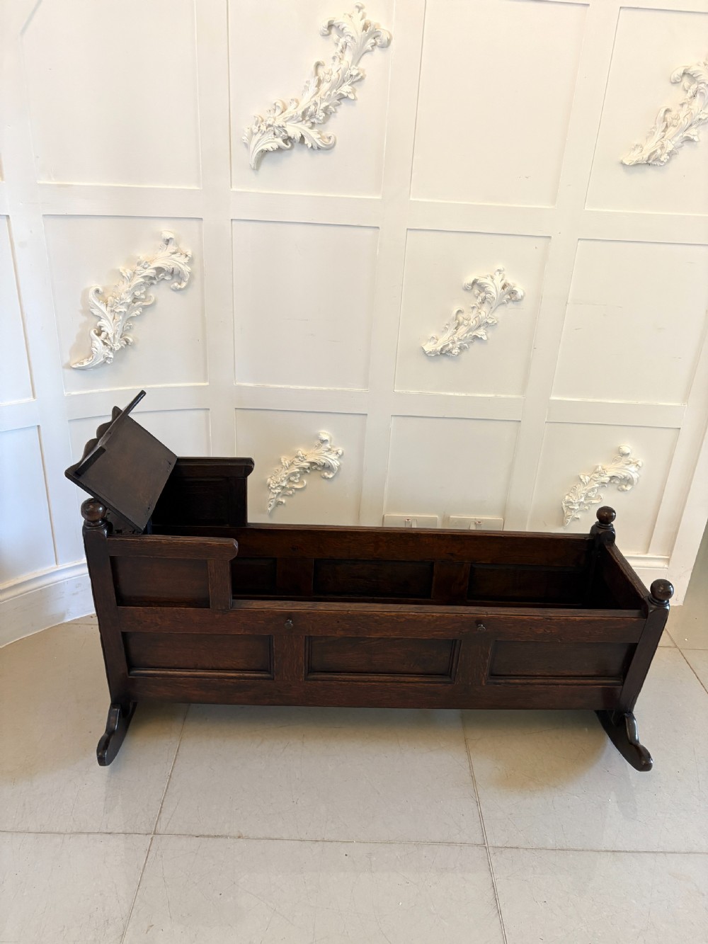 A dark oak panelled rocking crib featuring a hooded end, raised corner finials, and curved rocking runners. View VI