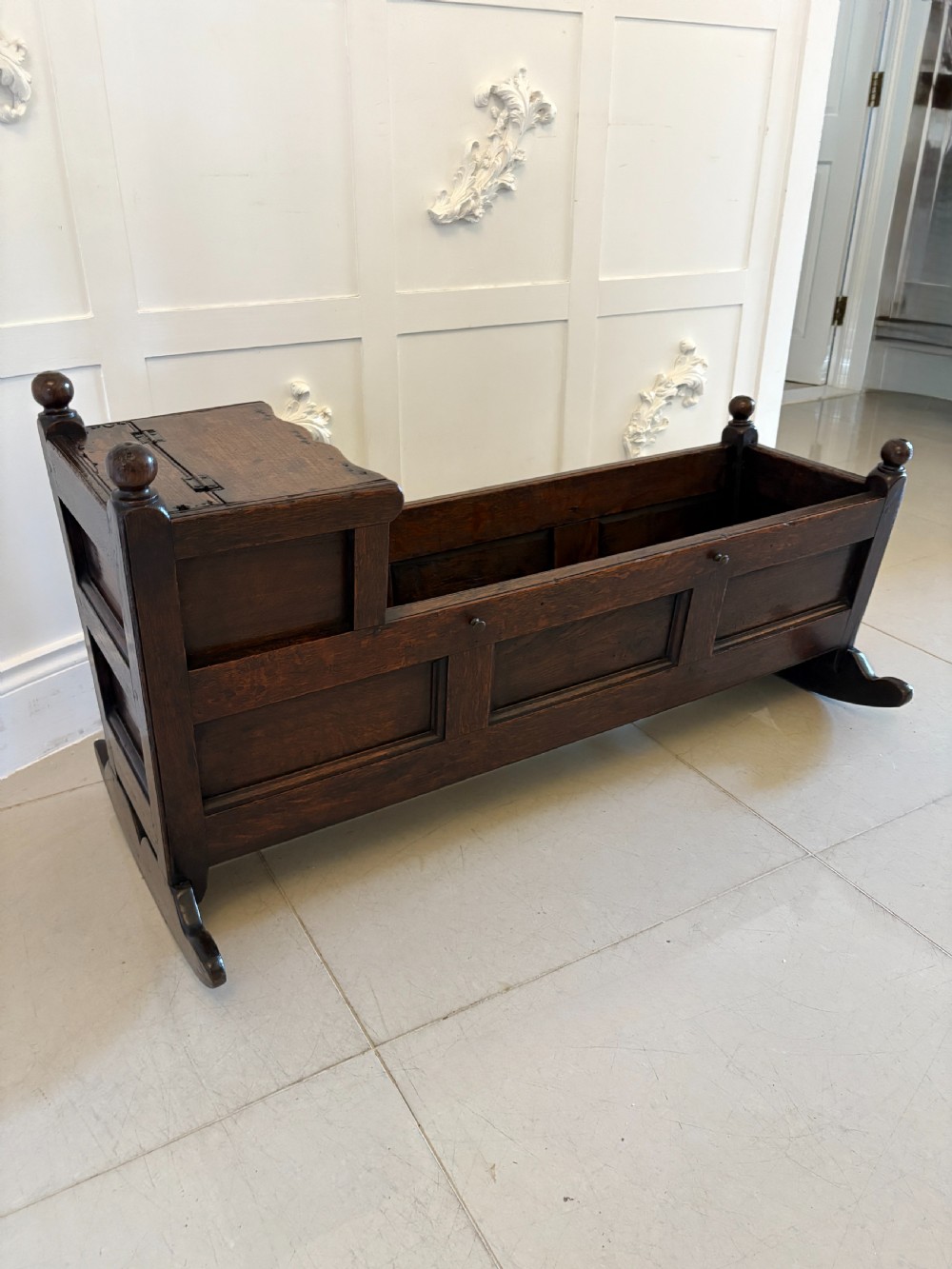A dark oak panelled rocking crib featuring a hooded end, raised corner finials, and curved rocking runners. View XII