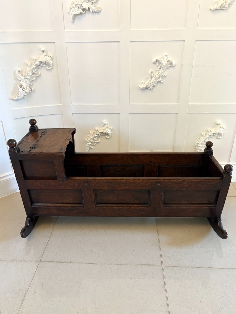 A dark oak panelled rocking crib featuring a hooded end, raised corner finials, and curved rocking runners. View XIII