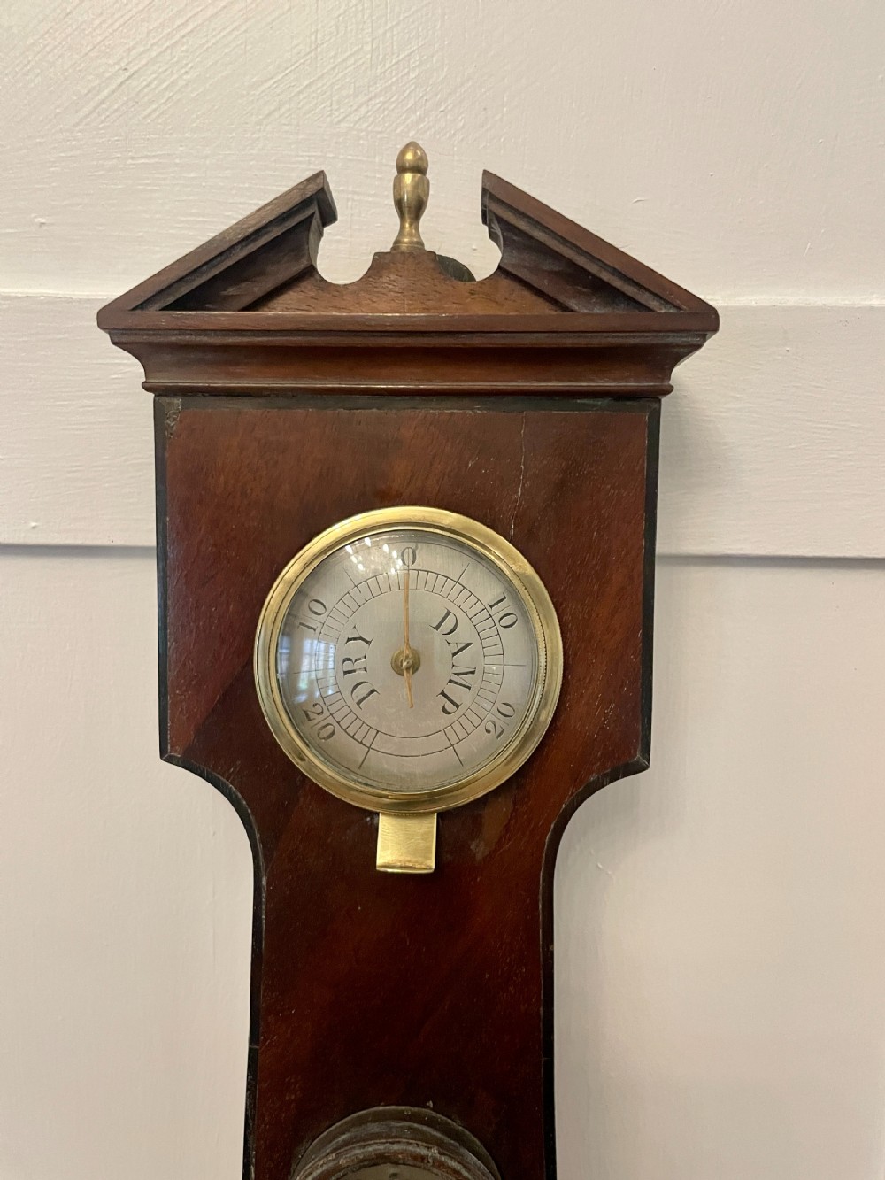 A vertical George III mahogany banjo barometer featuring a pediment top, glass thermometer tube, silvered dial, and brass bezel. View V