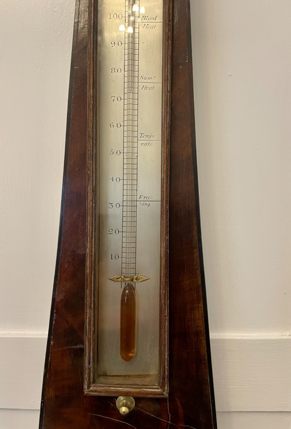 A vertical George III mahogany banjo barometer featuring a pediment top, glass thermometer tube, silvered dial, and brass bezel. View VI