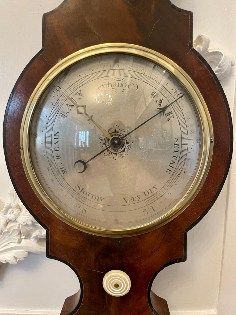 A vertical George III mahogany banjo barometer featuring a pediment top, glass thermometer tube, silvered dial, and brass bezel. View VII