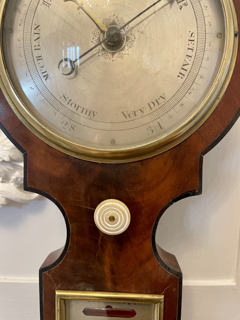 A vertical George III mahogany banjo barometer featuring a pediment top, glass thermometer tube, silvered dial, and brass bezel. View X