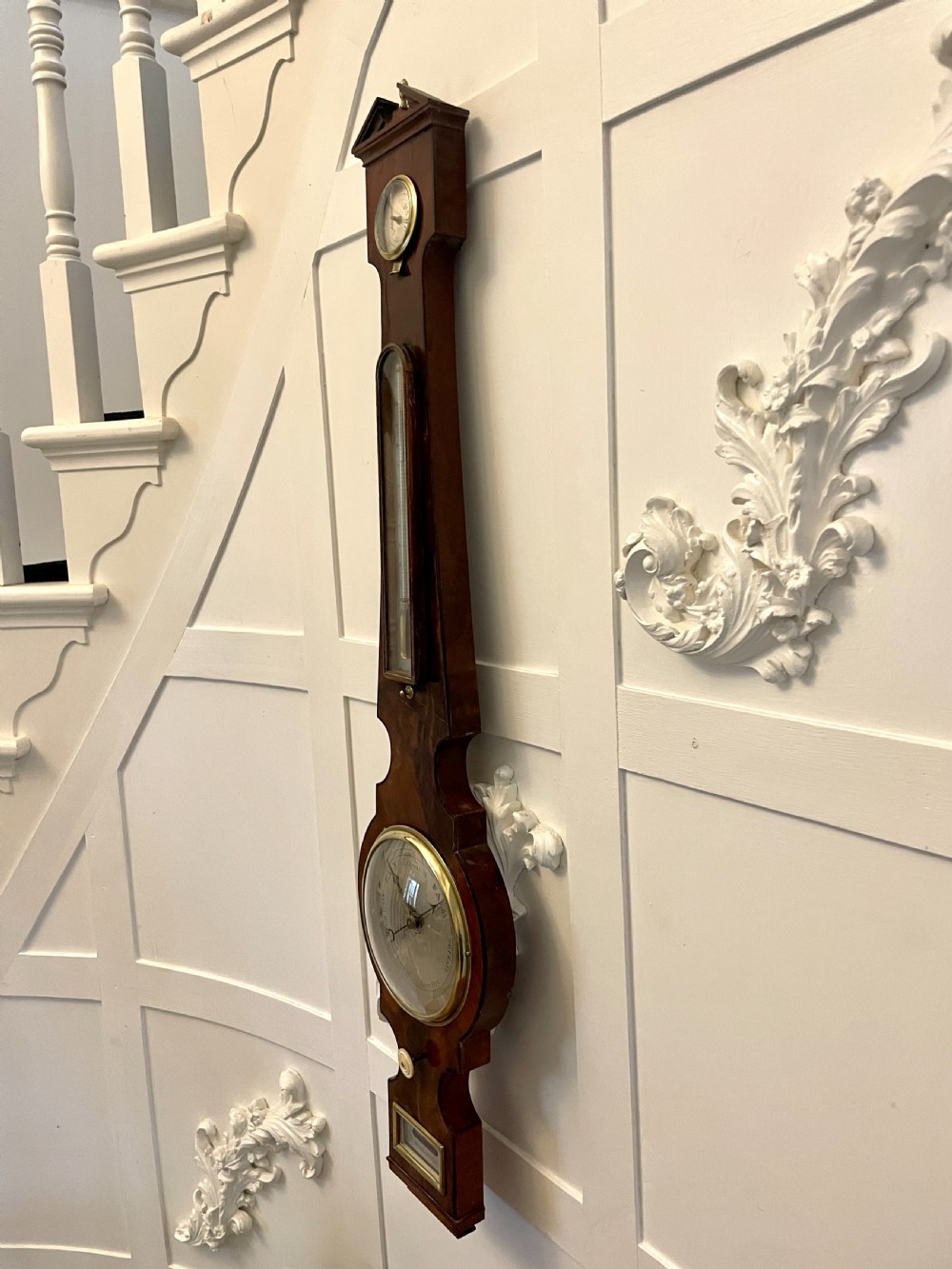 A vertical George III mahogany banjo barometer featuring a pediment top, glass thermometer tube, silvered dial, and brass bezel. View XI