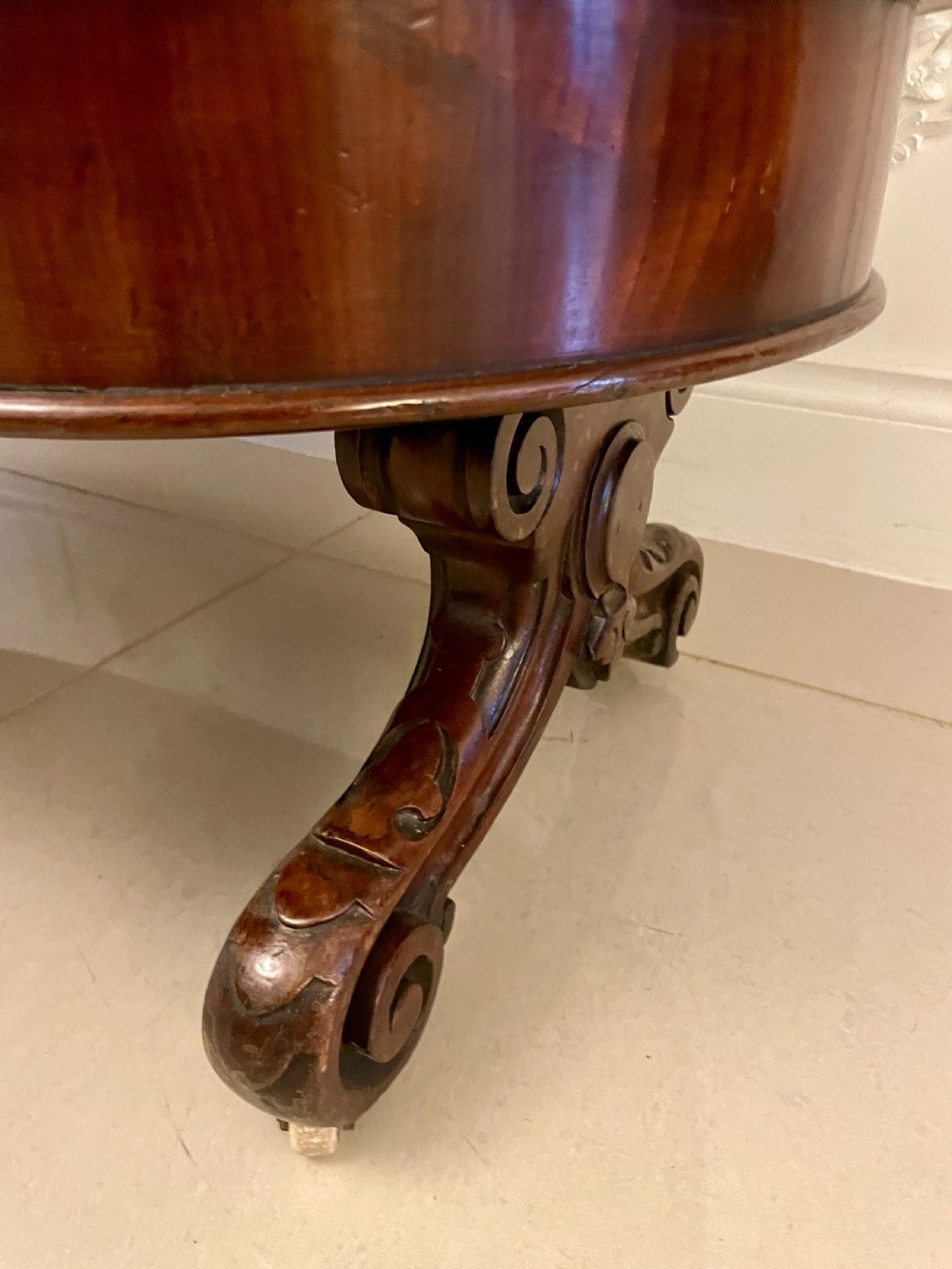An oval dark mahogany two-tiered serving table featuring turned support columns, metal scroll handles, and carved feet with casters. View IX