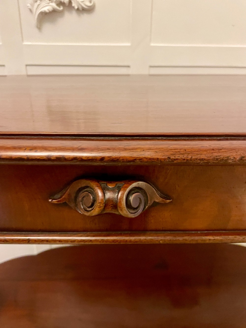 An oval dark mahogany two-tiered serving table featuring turned support columns, metal scroll handles, and carved feet with casters. View XI
