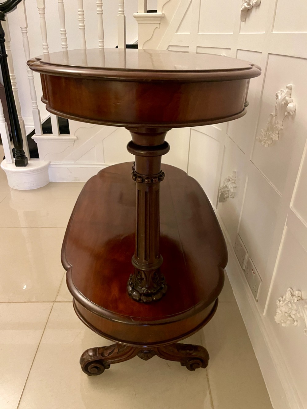 An oval dark mahogany two-tiered serving table featuring turned support columns, metal scroll handles, and carved feet with casters. View XIII