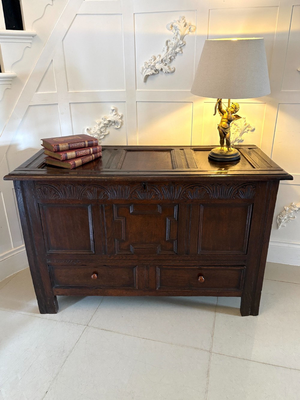 A seventeenth-century dark oak mule chest featuring a carved top frieze, geometric carved central panel, and two lower drawers with wooden turnings. View XXI