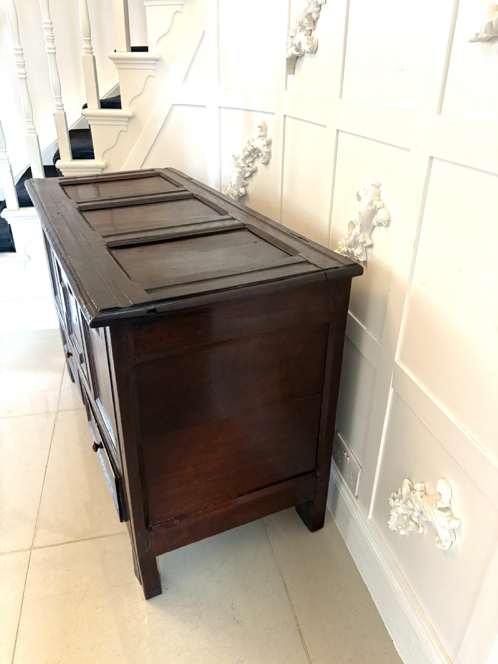 A seventeenth-century dark oak mule chest featuring a carved top frieze, geometric carved central panel, and two lower drawers with wooden turnings. View III