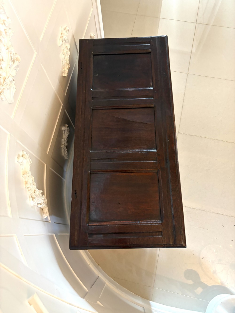 A seventeenth-century dark oak mule chest featuring a carved top frieze, geometric carved central panel, and two lower drawers with wooden turnings. View XI