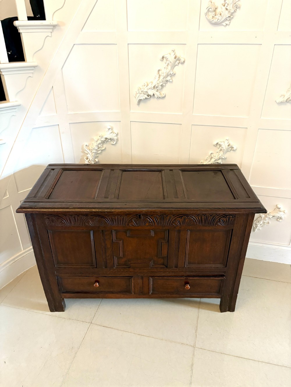A seventeenth-century dark oak mule chest featuring a carved top frieze, geometric carved central panel, and two lower drawers with wooden turnings. View XII