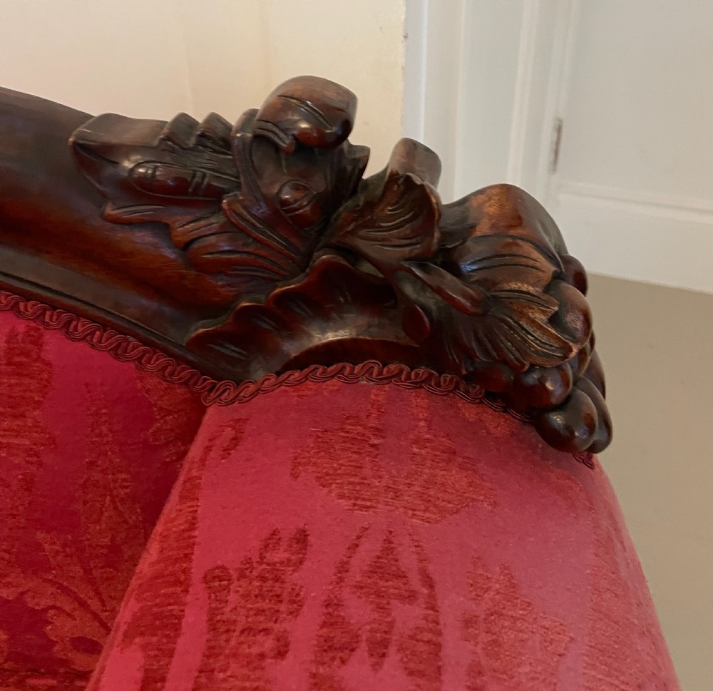 A Victorian carved mahogany chaise longue upholstered in patterned red damask fabric featuring an asymmetrical backrest and carved cabriole legs. View V
