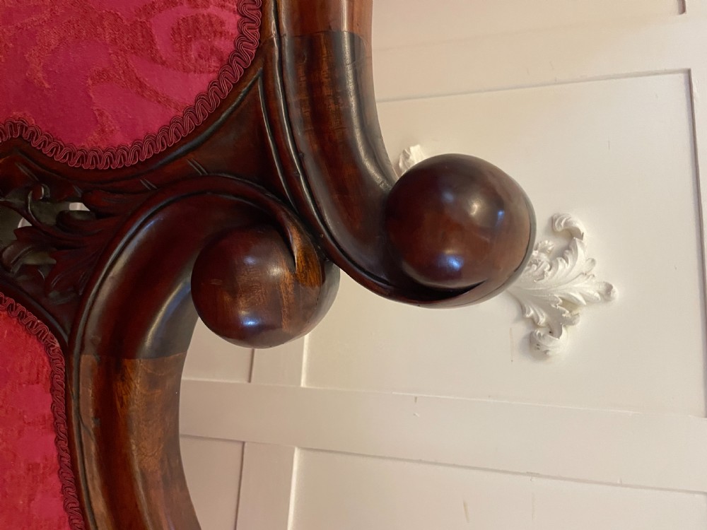A Victorian carved mahogany chaise longue upholstered in patterned red damask fabric featuring an asymmetrical backrest and carved cabriole legs. View VI