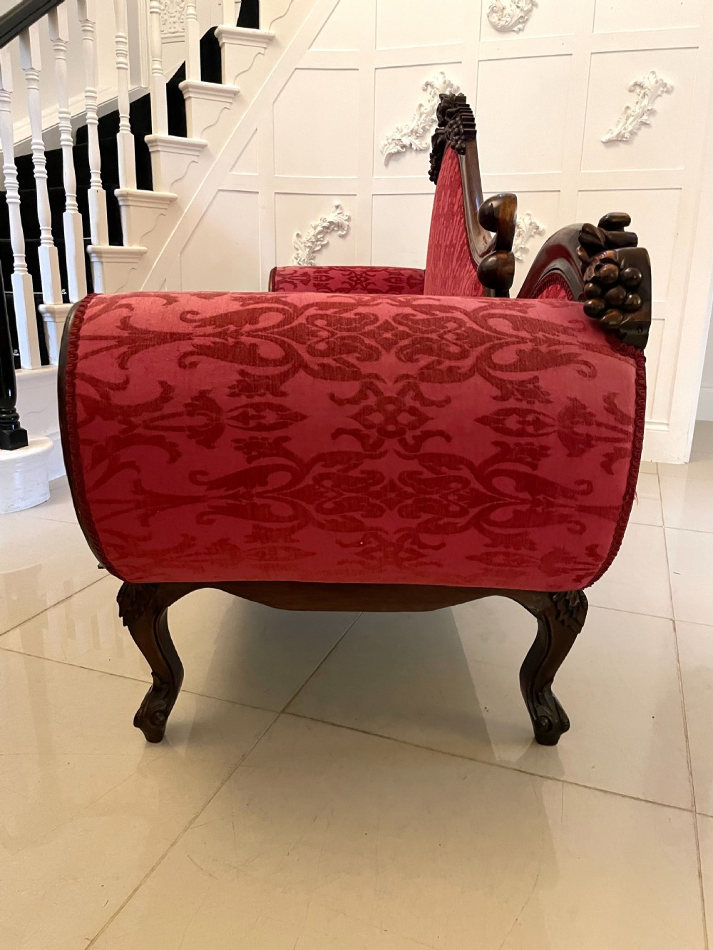 A Victorian carved mahogany chaise longue upholstered in patterned red damask fabric featuring an asymmetrical backrest and carved cabriole legs. View XV