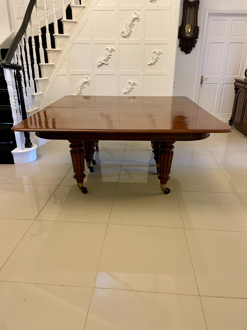 A long, highly polished Victorian mahogany dining table with rounded corners, inserted extension leaves, fluted turned legs, and brass castors. View IV