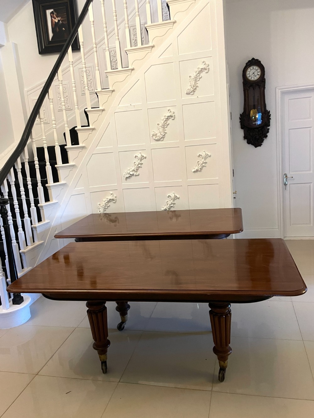 A long, highly polished Victorian mahogany dining table with rounded corners, inserted extension leaves, fluted turned legs, and brass castors. View VI