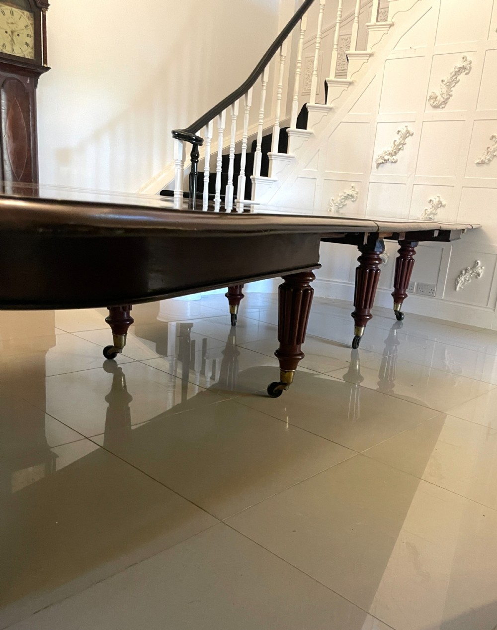 A long, highly polished Victorian mahogany dining table with rounded corners, inserted extension leaves, fluted turned legs, and brass castors. View IX