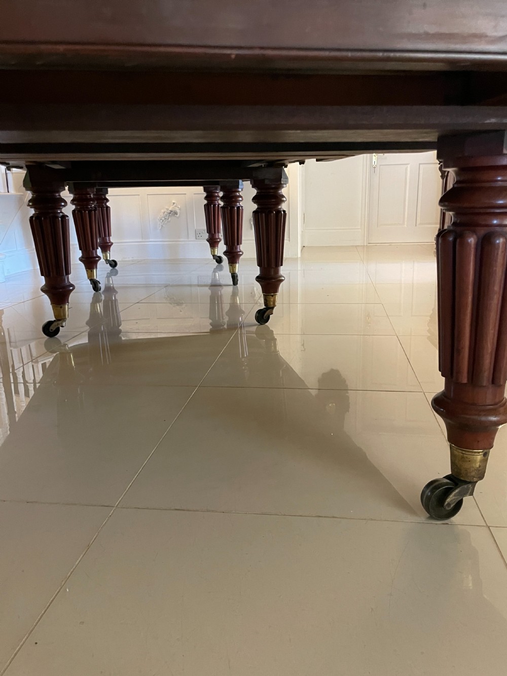A long, highly polished Victorian mahogany dining table with rounded corners, inserted extension leaves, fluted turned legs, and brass castors. View XII