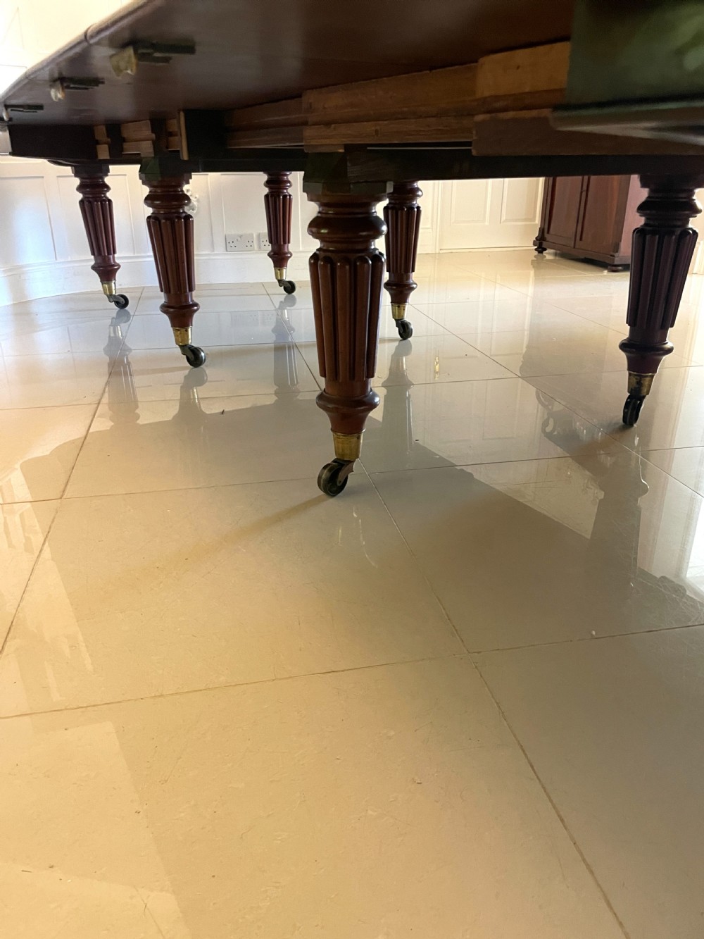 A long, highly polished Victorian mahogany dining table with rounded corners, inserted extension leaves, fluted turned legs, and brass castors. View XV