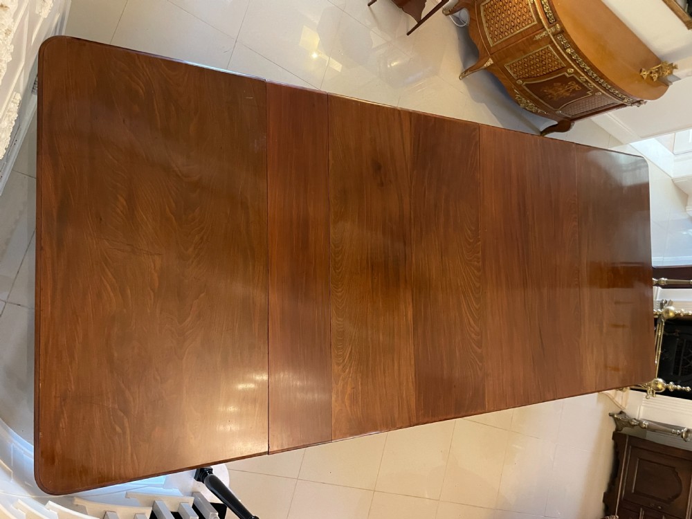 A long, highly polished Victorian mahogany dining table with rounded corners, inserted extension leaves, fluted turned legs, and brass castors. View XVI