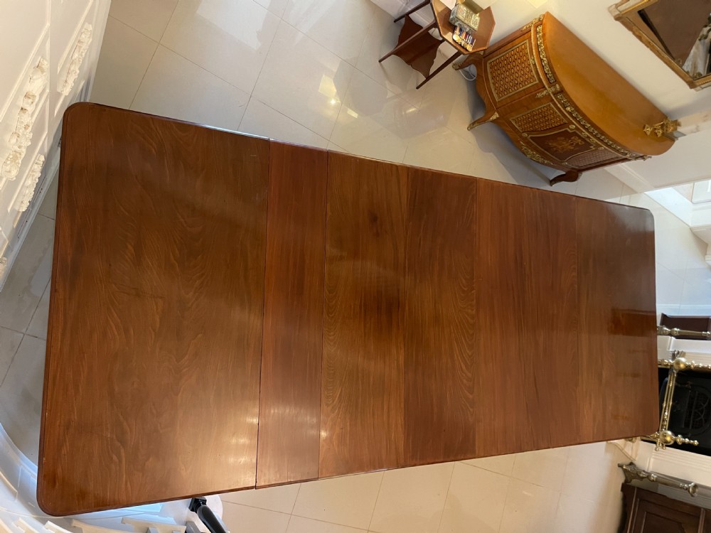 A long, highly polished Victorian mahogany dining table with rounded corners, inserted extension leaves, fluted turned legs, and brass castors. View XVII