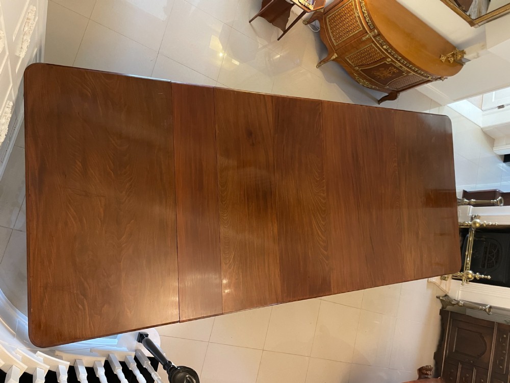 A long, highly polished Victorian mahogany dining table with rounded corners, inserted extension leaves, fluted turned legs, and brass castors. View XVIII