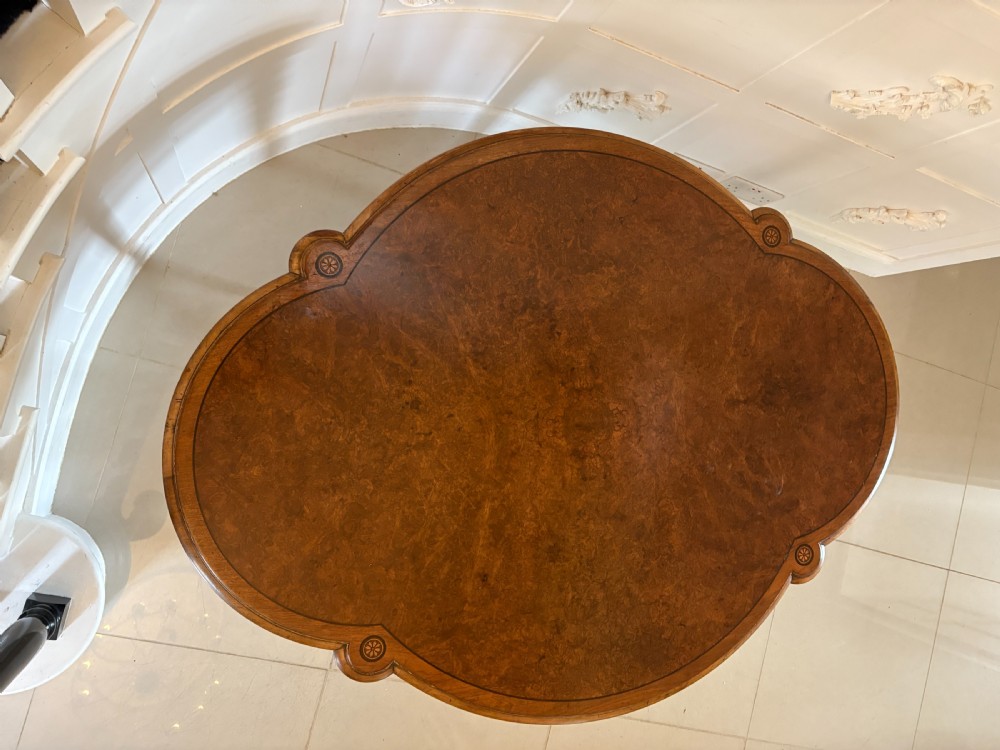 A Victorian burr walnut centre table with a lobed shaped top, inlaid crossbanding, turned legs, and an X-form stretcher on castors. View III