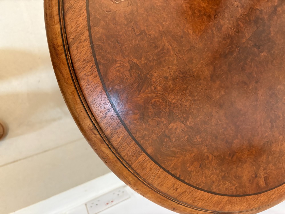 A Victorian burr walnut centre table with a lobed shaped top, inlaid crossbanding, turned legs, and an X-form stretcher on castors. View VI