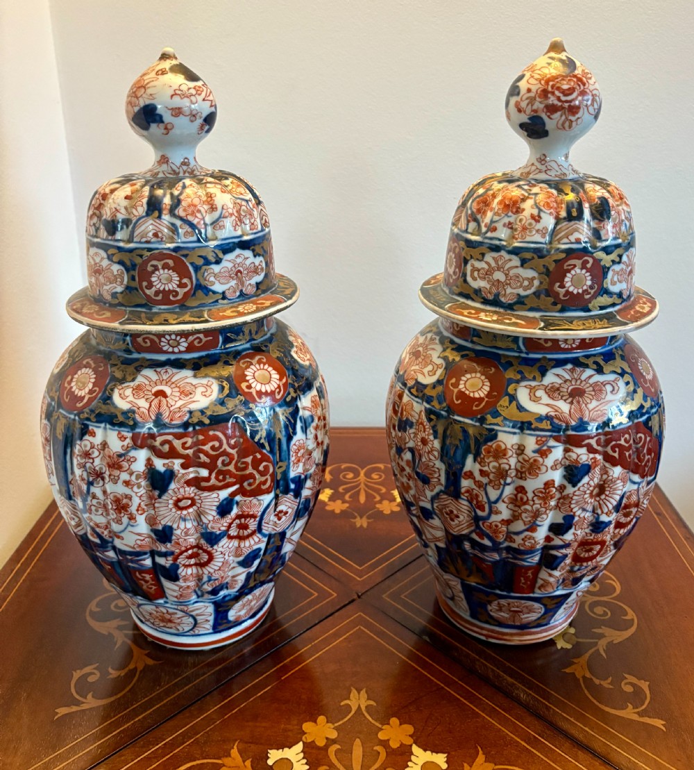 A pair of matching Japanese Imari lidded porcelain vases featuring fluted baluster bodies decorated with cobalt blue, iron-red, and gilded floral motifs.