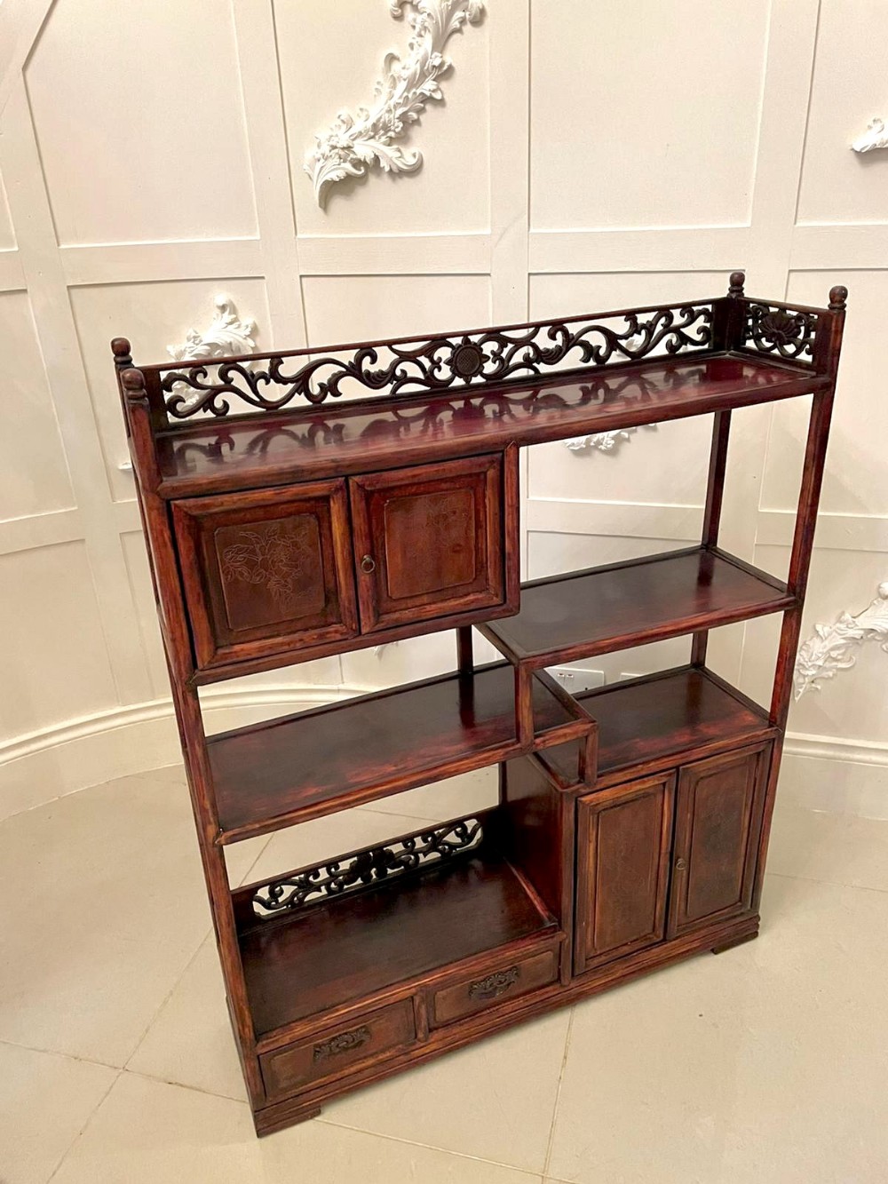 An antique Chinese hardwood display cabinet featuring asymmetrical open shelves, carved gallery rails, and small two-door cupboards.